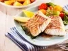 Fotografia mostra dois filés de peixe grelhado sobre um prato branco acompanhado de salada.