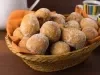 Em cima de uma mesa, cesta de palha com pano laranja com bolinhos de chuva, polvilhado com açúcar de confeiteiro.