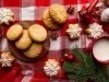 Em cima de uma mesa decorada de Natal, prato com biscoitos redondos e formado de estrelas crocantes, os em formato de estrela estão decorados com glacê branco.