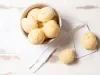 Imagem vista de ima de um bowl branco com pães de queijo. Ao lado, 2 pães de queijo sobre um pano branco.