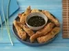 Foto da receita de Costelinha de Tilápia Copacol Empanada com Molho Oriental na Airfryer, servida em um tigela azul escura, com um pote pequeno com o molho no centro do prato, tudo numa bancada azul