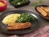 Imagem de um prato com um pedaço de banana frita, farofa e couve refogada. Ao lado, uma travessa com mais bananas fritas.