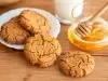 Em cima de uma mesa, prato branco com biscoitos crocantes, decorados com granulado de açúcar cristal. Ao lado do prato, pote com mel.