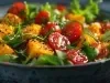 Em cima de uma mesa, tigela com folhas, manga cortada e tomates cerejas cortados ao meio, regado com molho.