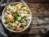 Fotografia de uma salada fresca em uma tigela branca sobre uma mesa de madeira rústica. A salada contém fatias de maçã, batatas cozidas, nozes, pedaços de maçã, um molho cremoso e salsa, apresentando um visual apetitoso.
