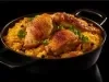 Panela preta com arroz cremoso amarelo com pedaços de cenoura, pedaços de frango e decorado com folhas de salsa.