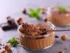 Imagem de um potinho redondo de vidro com mousse de chocolate e uma colher mostrando a textura cremosa da receita. Ao fundo, pedaços de chocolate e folhas de hortelã decorando.