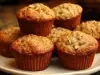 Nesta imagem, há uma pilha de muffins de banana com pedaços visíveis de nozes, colocados em um prato branco. A iluminação quente destaca a textura dourada dos bolinhos, que parecem úmidos e bem macios.
