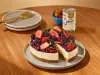 Fotografia mostra uma fatia de cheesecake de frutas vermelha sendo retirada e a lata de leite moça.