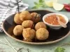 Imagem de um prato rústico preto com bolinhos de arancini e um potinho com geleia de pimenta.