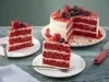 Imagem de dois pratos com fatias do bolo red velvet decorados com frutas vermelhas e ao fundo, o bolo inteiro.