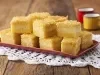 8 pedaços quadrados de bolo amarelo com uma lista branca no meio, dispostos em um prato vermelho que está em cima de uma toalha branca