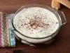 Em cima de uma mesa, recipiente redondo de vidro com creme de chocolate, decorado com chantilly e raspas de chocolate.