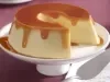 Imagem de um prato com pé branco com o pudim de leite condensado e calda de caramelo cortado.