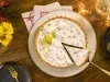 Imagem vista de cima de uma torta de limão com merengue e uma fatia sendo retirada. Ao redor, decoração de Natal.