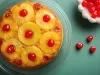 Fotografia vista de cima de uma torta inteira com rodelas de abacaxi caramelizados, a torta está sobre um apoio de vidro e apoiado em uma mesa de tom verde azulado.