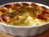 Em cima de uma mesa, refratário branco  com batatas e queijo gratinado e um creme branco com bacalhau desfiado.