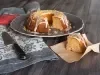 Fotografia de um bolo de bundt parcialmente fatiado, exibindo sua textura densa e úmida. Coberto com um glacê brilhante e raspas de limão, está disposto em um prato escuro, ao lado de uma faca e sobre um pano decorativo.