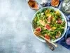 Em cima de uma mesa, prato com salada com mix de folhas, frutas em cubos e figo.