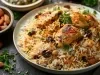 Em cima de uma mesa, prato branco redondo com arroz soltinho, cenoura, uvas-passas, amendôas e frango picado, decorado com folhas de salsa.