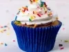 Imagem de um cupcake em forma branca, decorado com chantily branco e granulados coloridos.