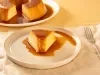 Imagem de um prato claro rústico com uma fatia de pudim de pão e calda de caramelo. Ao fundo, um prato com o restante do pudim.