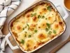 Em cima de uma mesa, refratário com batatas com queijo gratinado, decorado com cheiro-verde picado.