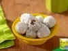 Doces de aveia em formato de bolinhas, cobertos com açúcar, dispostos em prato amarelo sobre mesa de madeira.
