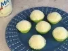 Seis brigadeiros brancos em forminhas verdes sobre prato azul decorado, com latas de LEITE MOÇA® ao fundo.