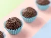 Imagem de brigadeiros enfileirados cobertos com chocolate granulado na forminha azul claro.