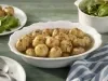 Fotografia em tons de azul em uma bancada de madeira verde, um pano branco com listras azuis, um recipiente oval branco com várias batatas bolinhas com pimenta calabresa.