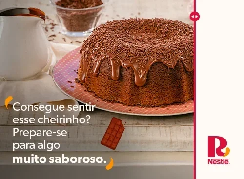 Bolo de chocolate com cobertura e granulado em prato rosa, jarra ao lado e texto sugerindo que uma novidade está por vir.