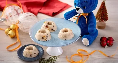 Manjar em prato azul claro com frutas secas, decoração natalina e mascote azul de Mucilon ao lado