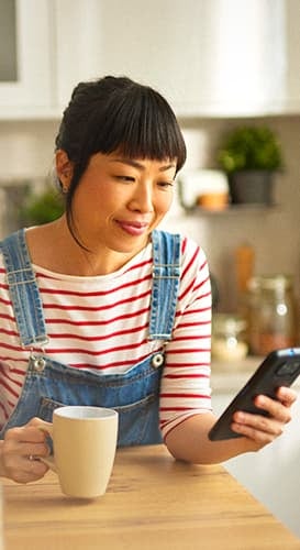  Mulher
              empreendedora sorrindo enquanto gerencia seu negócio pelo smartphone em sua cozinha.