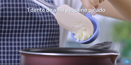 Pessoa joga alho picado de uma colher medidora na panela
