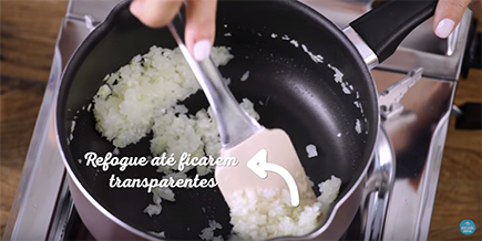 Pessoa mexe cebola e alho na panela com uma espátula