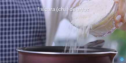 Pessoa joga arroz branco de uma xícara na panela