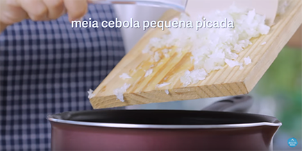 Pessoa joga cebolas picadas de uma tábua na panela
